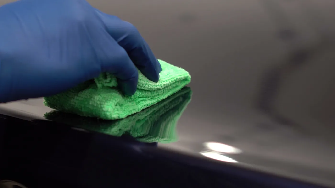 A gloved technician pressing a microfiber applicator onto a black glossy fender